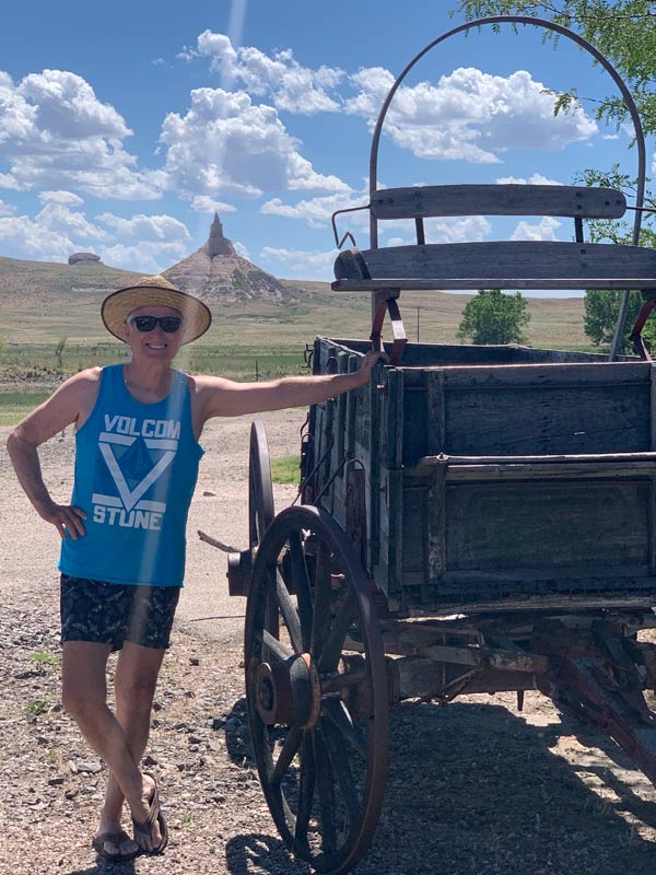 John beside a wagon with Chimney Rock in Western Nebraska in the background